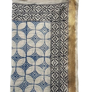 May include: A white cotton fabric with a blue and black geometric pattern. The fabric has a gold trim on the right side.