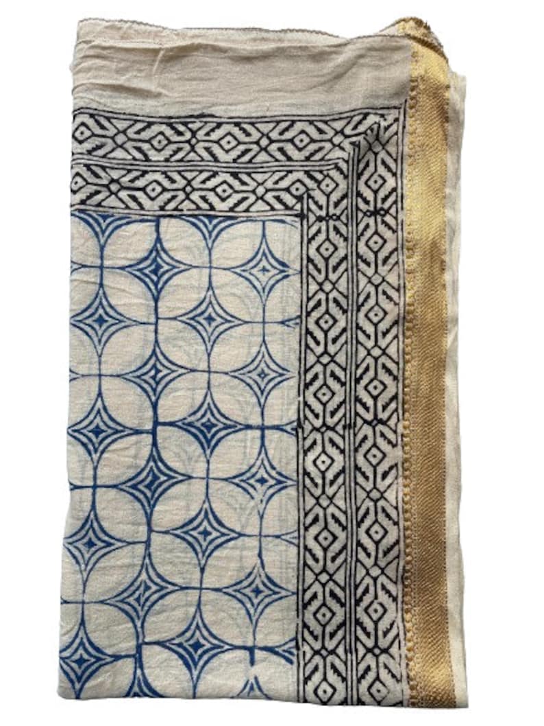 May include: A white cotton fabric with a blue and black geometric pattern. The fabric has a gold trim on the right side.