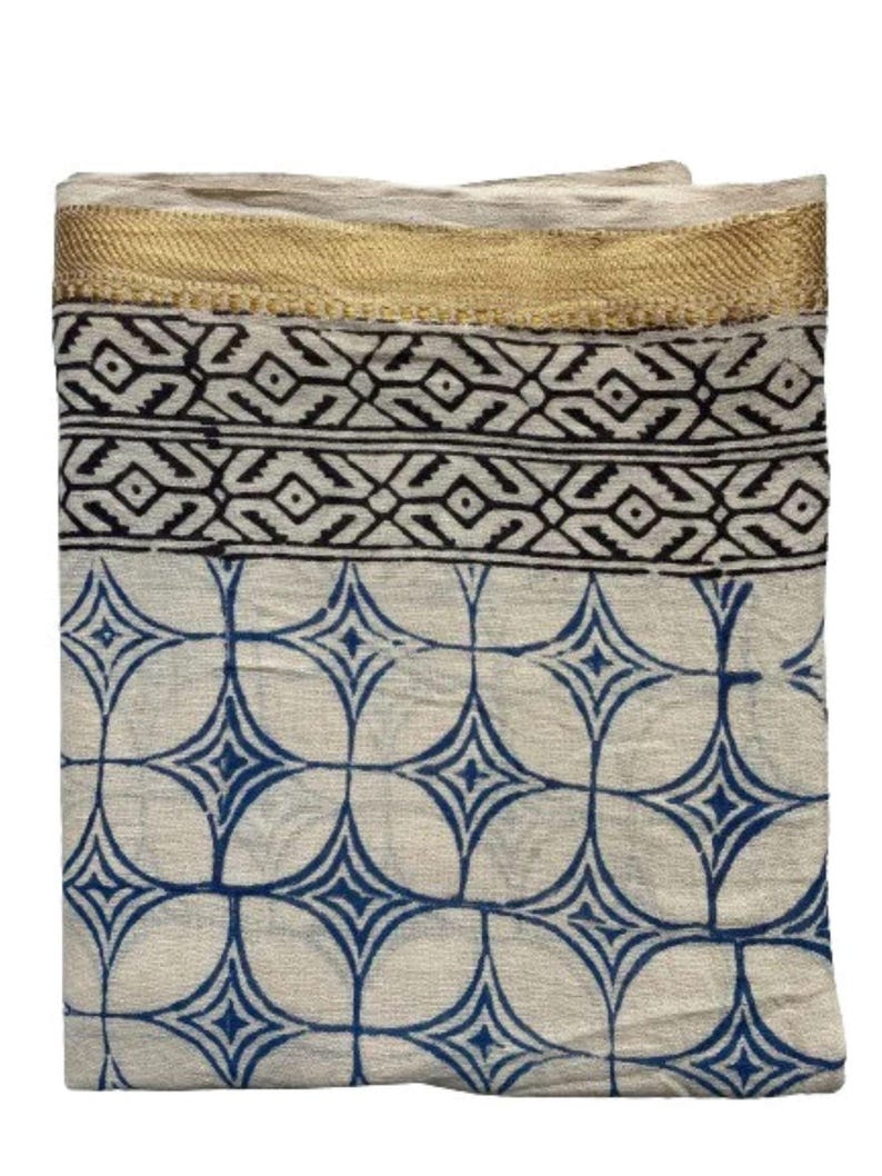May include: A white cotton scarf with a blue and white geometric pattern and a gold trim.