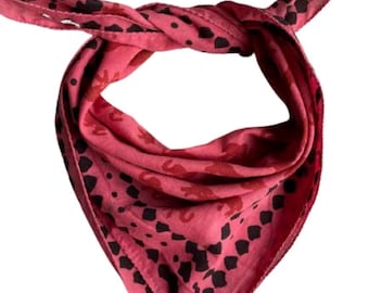 May include: A pink bandana with a black and red patterned design. The bandana is folded and tied in a knot.