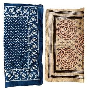 May include: Two fabric squares with different patterns. The square on the left is blue with a white geometric pattern and white floral designs. The square on the right is beige with a brown geometric pattern and red circles.