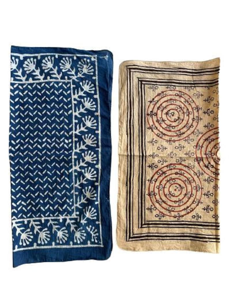 May include: Two fabric squares with different patterns. The square on the left is blue with a white geometric pattern and white floral designs. The square on the right is beige with a brown geometric pattern and red circles.