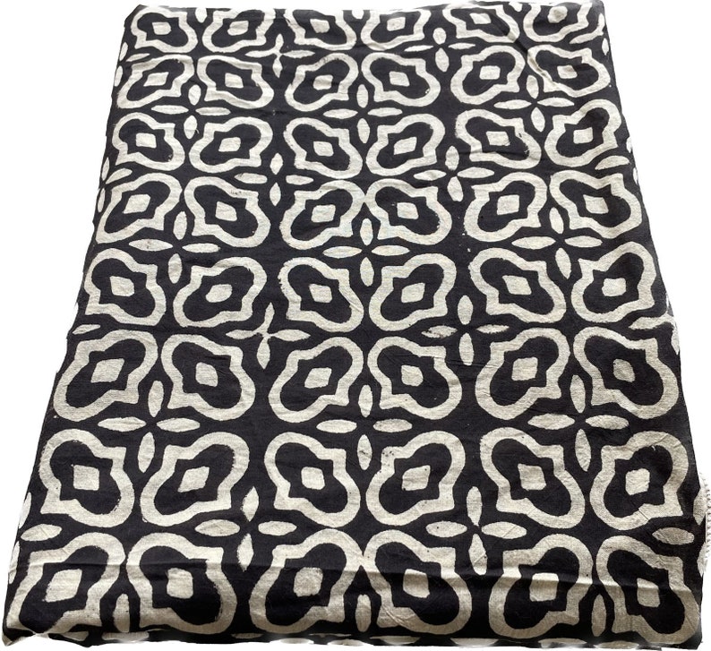 May include: Black and white fabric with a repeating geometric pattern. The pattern is made up of stylized flowers with rounded edges.