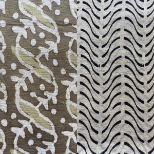 May include: Close-up of a textile with two distinct patterns. One side features white leaf and dot designs on a brown background. The other side has black wavy lines on a beige background. The fabric has a textured appearance.