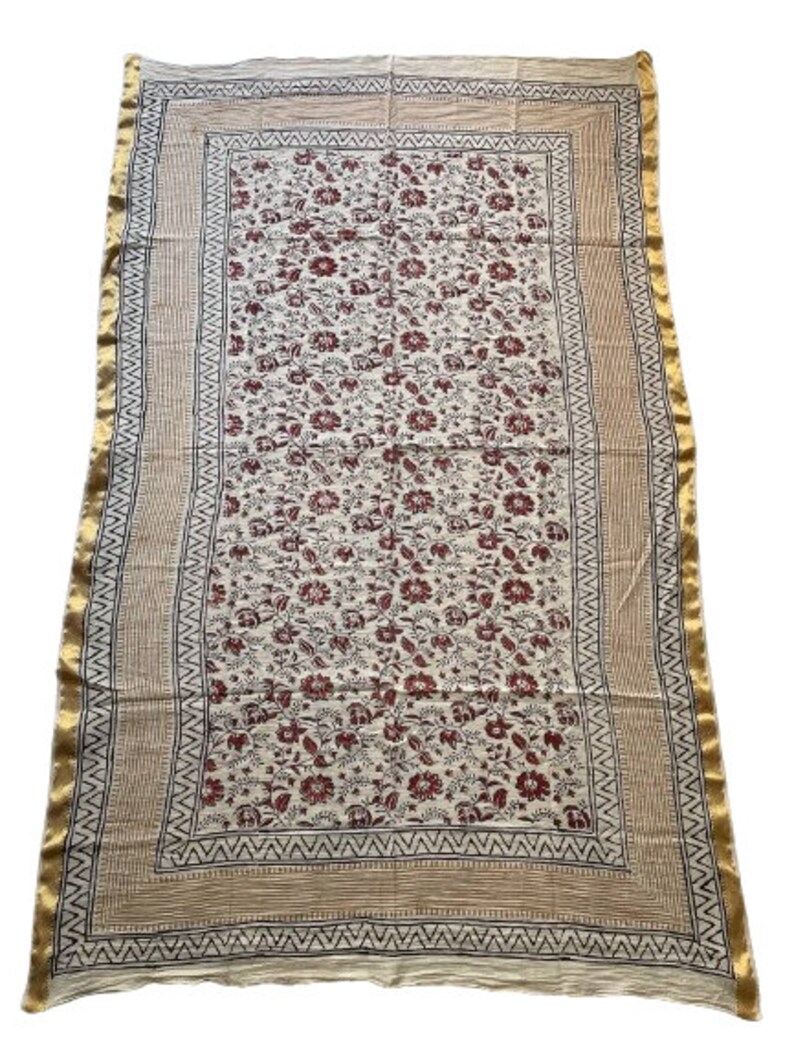 May include: A white cotton fabric with a red floral print and a gold border. The fabric has a traditional Indian design.