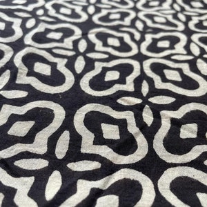May include: Black and white fabric with a repeating pattern of stylized flowers. The fabric has a textured surface.