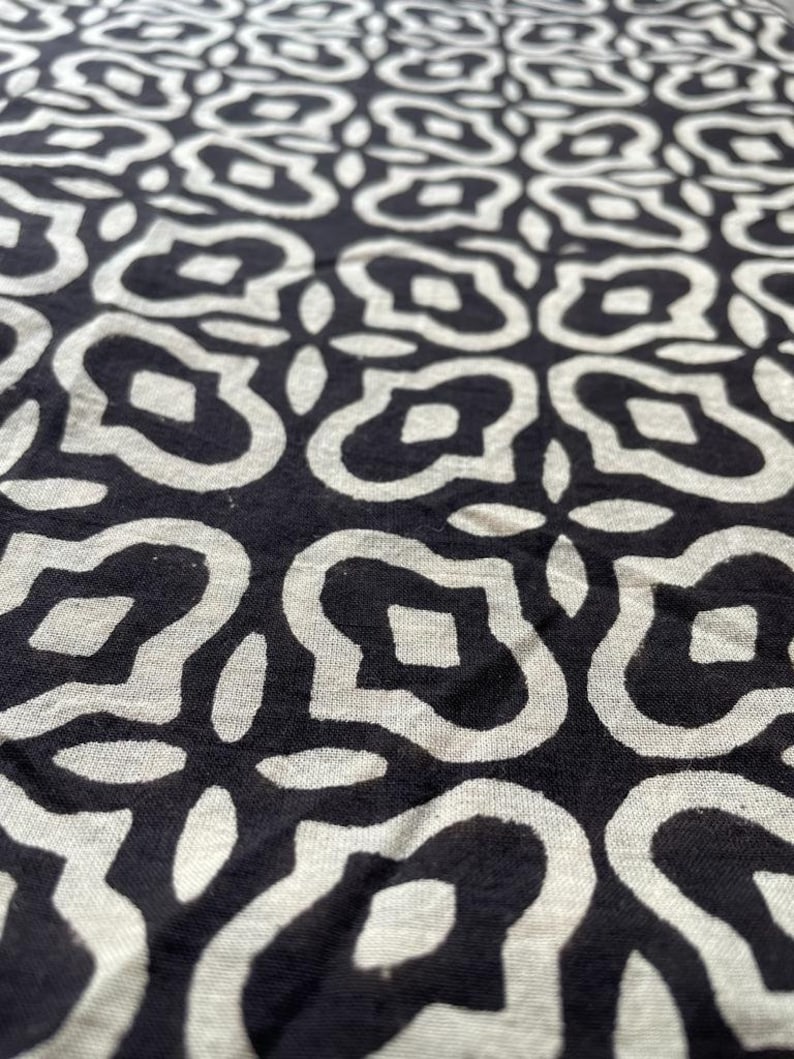 May include: Black and white fabric with a repeating pattern of stylized flowers. The fabric has a textured surface.