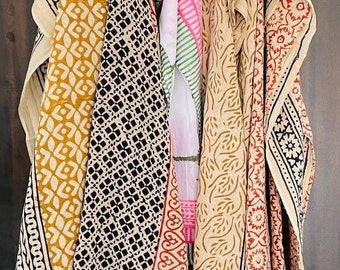 May include: Five different cotton fabric squares with block printed designs in shades of brown, black, red, and white. The fabric squares are hanging on a wooden rod.