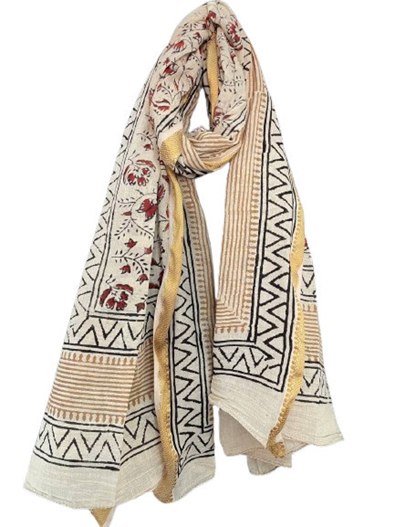May include: A white cotton scarf with a floral print in shades of red and brown. The scarf has a gold border and a geometric pattern in black and brown.