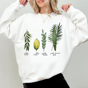 Może przedstawiać: Biała bluza z nadrukiem czterech gatunków używanych w żydowskim święcie Sukkot. Gatunki są oznaczone po hebrajsku i angielsku: wierzba, etrog, mirt i gałąź palmowa.