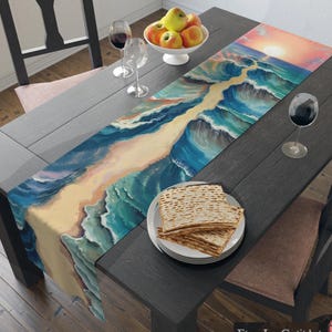 May include: A table runner with a painted image of the parting of the Red Sea. The runner is on a dark wood table with a bowl of apples, two glasses of wine, and a plate of matzah.