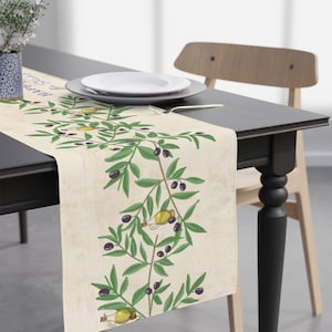 May include: A beige table runner with a green olive branch design. The runner features a repeating pattern of olive branches with black olives and yellow olive oil bottles. The text "Happy & Healthy" is printed on the runner.