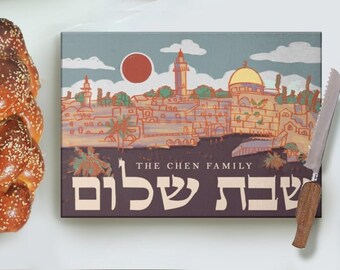 May include: A brown cutting board with a colorful illustration of the Jerusalem skyline, including the Dome of the Rock. The text "THE CHEN FAMILY" and "שבת שלום" are printed on the board.