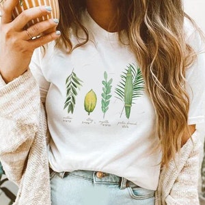 Puede incluir: Camiseta blanca con un gráfico de las cuatro especies utilizadas en la festividad judía de Sucot. Las especies están etiquetadas en hebreo e inglés: sauce, etrog, mirto y rama de palma.
