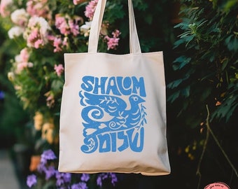 Könnte beinhalten: Eine weiße Canvas-Tragetasche mit blauem Text und einem blauen Taubenmotiv. Der Text lautet "Shalom" und "שלום".