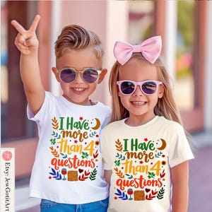 May include: Two children wearing white t-shirts with the text "I Have More Than 4 Questions" printed on them. The shirts feature a colourful floral design with a crescent moon and stars. The children are wearing sunglasses and smiling.