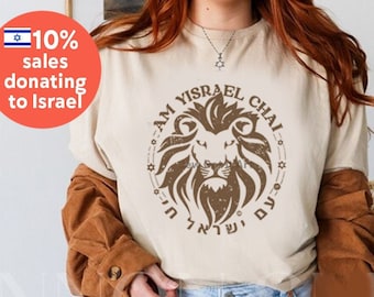 Op de afbeelding: Een beige T-shirt met een bruine leeuwenafbeelding en de tekst "Am Yisrael Chai" in het Hebreeuws en Engels. De afbeelding is verweerd en heeft een vintage uitstraling.