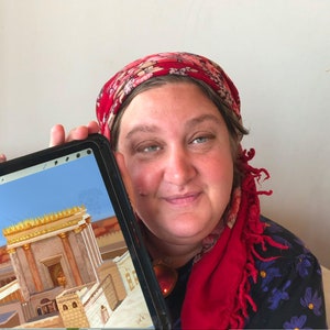 May include: A woman wearing a red headscarf holds a tablet showing a 3D rendering of a golden temple.