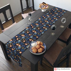 Pode incluir: Um corredor de mesa azul e dourado com um padrão de mãos de hamsa, menorás e romãs. O corredor está sobre uma mesa de madeira escura com uma tigela de donuts e dois copos de vinho.
