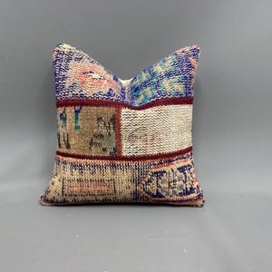 May include: A square throw pillow with a patchwork design featuring various shades of blue, red, and beige. The pillow is made of woven fabric with a textured surface.