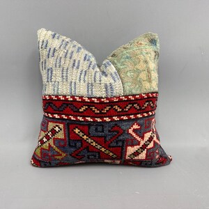 May include: A small, square cushion with a patchwork design. The cushion is made of different fabrics with various patterns, including a blue and white striped fabric, a green and white floral fabric, and a red and blue geometric fabric.