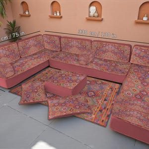 May include: A U-shaped seating set with a patterned design in shades of red, orange, and blue. The set includes a corner sofa, a long sofa (330 cm / 130 in), a square ottoman, and several cushions. The set is 190 cm / 75 in wide and 70 cm / 28 in deep.