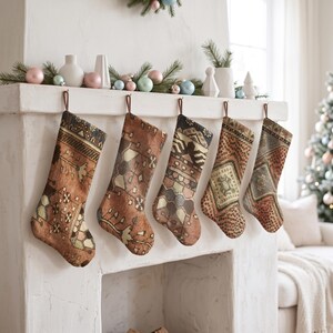 May include: Five Christmas stockings hanging in a row from a white fireplace mantel. Each stocking features a unique, intricate woven pattern in shades of brown, tan, and muted blue, resembling traditional rug designs with geometric motifs.
