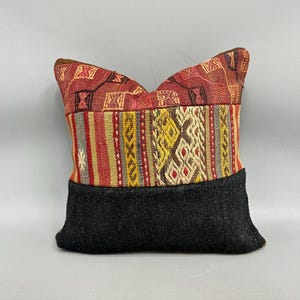 May include: A decorative pillow with a black fabric backing and a colorful patterned front. The pattern features red, yellow, and blue geometric shapes.