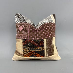 May include: A patchwork pillow with a brown, pink, and white color scheme. The pillow is made of different fabrics with various patterns, including stripes, polka dots, and geometric designs.
