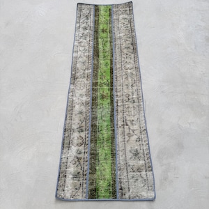 May include: A long, narrow rug with a green stripe down the center. The rug has a faded, vintage look and is bordered with a light blue trim.