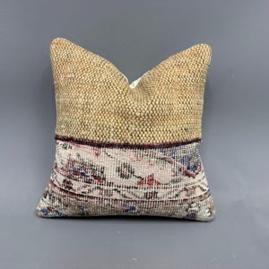 Pode incluir: Uma almofada bege e marrom com um inserto de tecido estampado. A almofada tem uma textura tecida e um design floral.