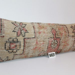 May include: A long, rectangular pillow with a beige background and a colorful floral pattern. The pillow has a traditional Turkish kilim design with red, black, and white accents. The pillow is labeled with the number 6021.
