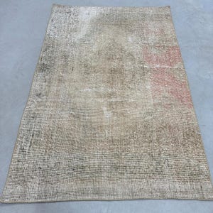 May include: A vintage-style rug with a faded, distressed look. The rug has a beige background with subtle brown and pink accents. The rug is made of a woven material and has a slightly textured surface.