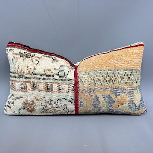 Könnte beinhalten: Ein rechteckiges Kissen mit Patchwork-Muster. Das Kissen ist aus cremefarbenem Stoff mit rotem Rand und zeigt verschiedene Muster in Braun-, Blau- und Grüntönen.