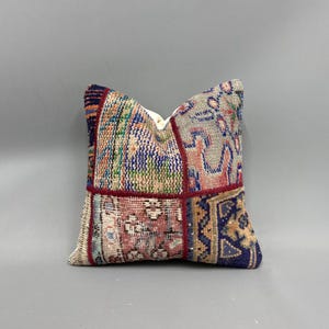 May include: A square throw pillow with a patchwork design. The pillow is made of different pieces of fabric with various patterns and colors, including red, blue, green, and beige.