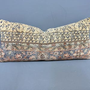 May include: Rectangular decorative pillow with a vintage rug design. The pillow features a cream-colored background with intricate floral and geometric patterns in shades of blue, brown, and red. The pillow is approximately 24 inches long.