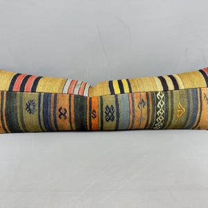 May include: A long, rectangular pillow with a patchwork design. The pillow features a yellow background with stripes of black, red, orange, blue, and green. The pillow is approximately 36 inches long.