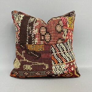Könnte beinhalten: Ein quadratisches Zierkissen mit Patchwork-Design. Das Kissen weist eine Mischung aus Farben auf, darunter Braun, Rot, Rosa, Gelb und Orange. Das Design umfasst geometrische Muster und strukturierten Stoff.