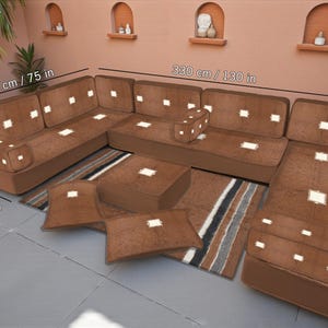 Puede incluir: Un juego de sofá seccional marrón con una otomana, cojines y alfombra a juego. El sofá mide 330 cm de largo y 190 cm de ancho, con una profundidad de asiento de 70 cm. El juego incluye una alfombra con rayas y detalles blancos.