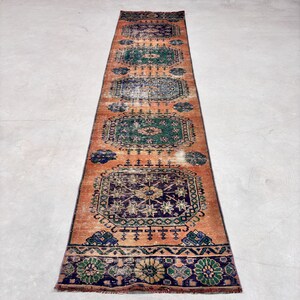 May include: An orange and blue runner rug with a distressed, vintage appearance. The rug features repeating geometric patterns in shades of blue, green, and orange. The rug is rectangular and appears to be made of woven material.