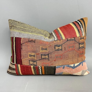 May include: A colorful patchwork pillow with a geometric pattern in shades of red, brown, green, and blue. The pillow is made of woven fabric and has a rustic, vintage look.