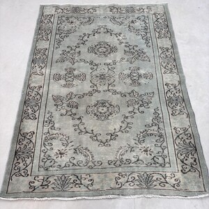 Puede incluir: Una alfombra vintage con fondo azul claro y un patrón floral negro. La alfombra tiene un borde con flecos.