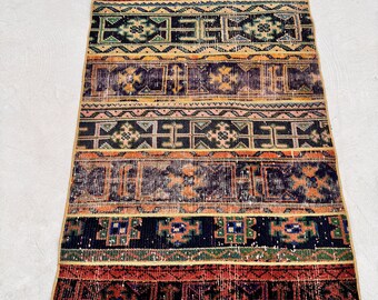 Puede incluir: Una alfombra vintage con un patrón geométrico colorido en tonos de rojo, naranja, amarillo, verde, azul y negro. La alfombra tiene un aspecto desgastado y está hecha de lana.