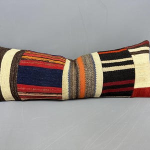 May include: Rectangular decorative pillow with a patchwork design. The pillow features sections of brown, cream, navy, red, orange, and black stripes. The pillow is a long, bolster style.