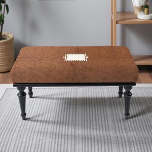 May include: A rectangular coffee table with a brown, textured top and black legs. The table has a decorative white design in the center. The legs are turned and have a classic design.