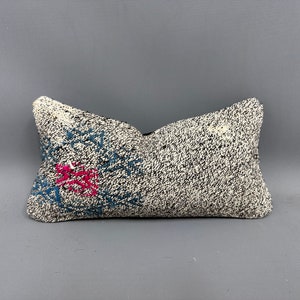 May include: A white and black patterned pillow with a pink and blue design. The pillow is made of a soft, textured fabric.