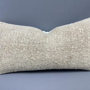 Pode incluir: Uma almofada bege retangular de tecido tecido texturizado. A almofada é retangular e tem uma costura branca no centro.