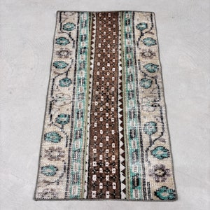 May include: A vintage rug with a brown, green and white geometric pattern. The rug has a faded look and is made of wool.