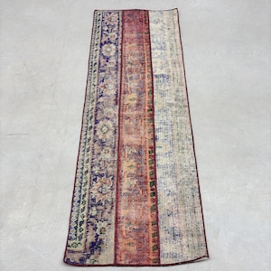 May include: A vintage runner rug with a faded, distressed look. The rug has a long, narrow shape and features a colorful striped pattern with intricate floral designs. The colors are muted and include shades of red, orange, blue, and green.