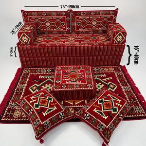 Puede incluir: Un juego de asientos de suelo rojo con un sofá (190 cm de ancho, 70 cm de alto, 20 cm de profundidad), dos cojines, una otomana cuadrada pequeña y dos alfombras. El conjunto presenta diseños geométricos.